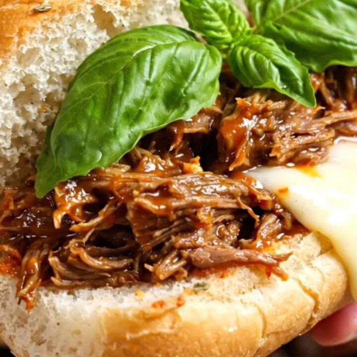 A close-up of a cheesy, pepperoni-topped shredded beef sub sandwich on a wooden board.