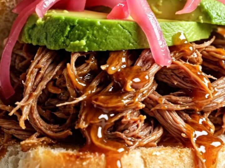 A close-up of a honey chipotle pulled beef torta on a rustic plate with visible steam.