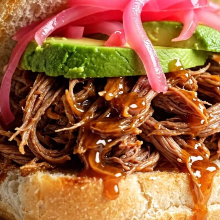 A close-up of a honey chipotle pulled beef torta on a rustic plate with visible steam.