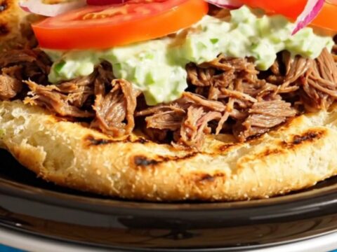 A close-up of shredded Greek beef inside a Crockpot, showing steam rising and seasoned meat.