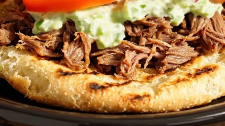 A close-up of shredded Greek beef inside a Crockpot, showing steam rising and seasoned meat.