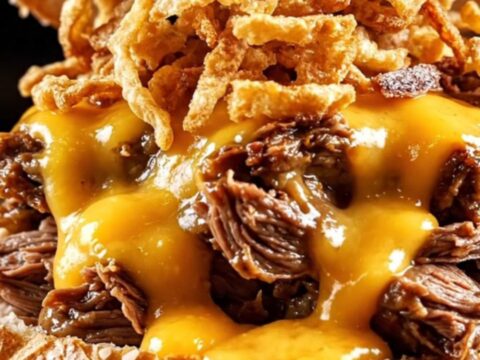 A close-up shot of a shredded beef sandwich on a pretzel bun with beer cheese sauce dripping down the sides.