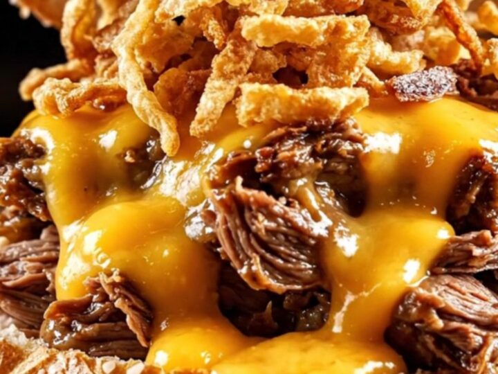 A close-up shot of a shredded beef sandwich on a pretzel bun with beer cheese sauce dripping down the sides.