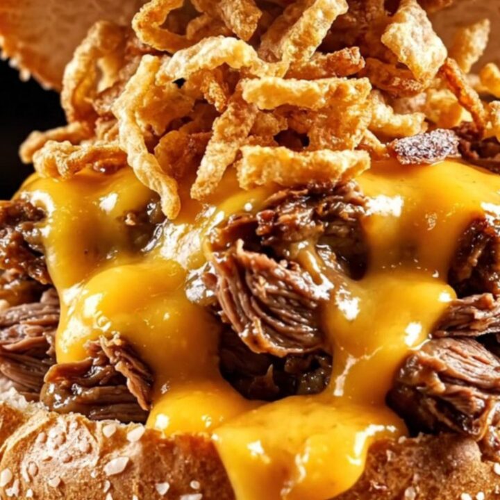 A close-up shot of a shredded beef sandwich on a pretzel bun with beer cheese sauce dripping down the sides.