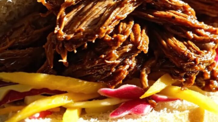 A close-up of tender, slow-cooked Jamaican jerk shredded beef served in a warm coco bread roll with fresh mango slaw.