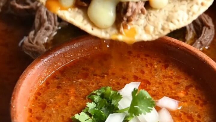 Close-up of a crispy quesataco being dipped into a bowl of rich, red birria consommé.