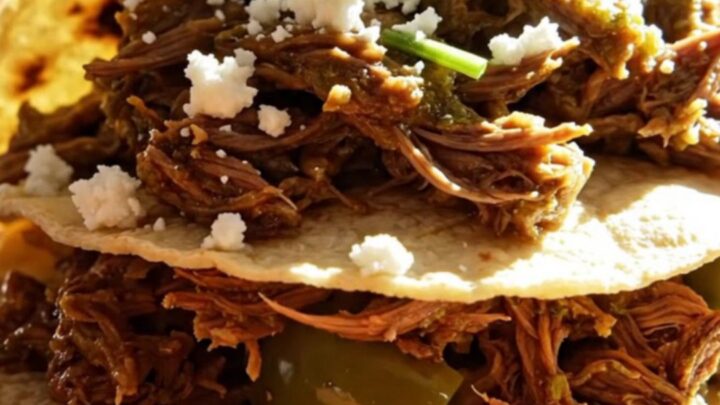 A close-up of tender, shredded beef in a vibrant green tomatillo sauce inside a ceramic slow cooker.