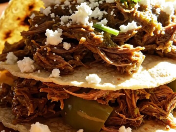 A close-up of tender, shredded beef in a vibrant green tomatillo sauce inside a ceramic slow cooker.
