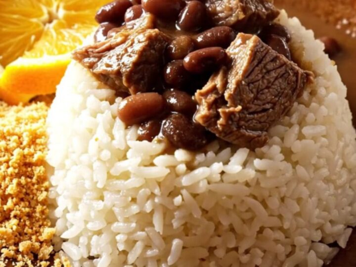 A steaming bowl of Brazilian Feijoada featuring tender beef, black beans, and orange slices, served over fluffy white rice.