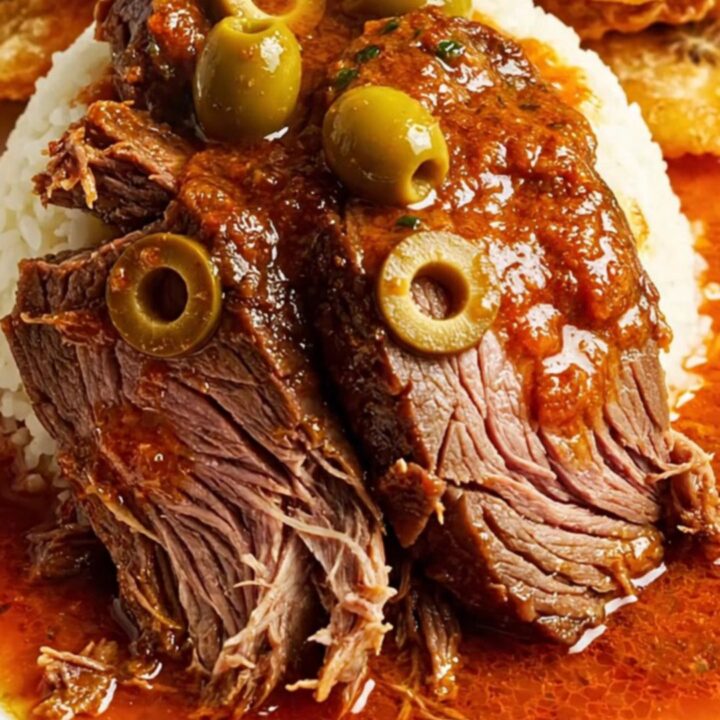 A close-up of a slow-cooked Carne Mechada beef roast sliced on a plate with vibrant green olives visible inside.