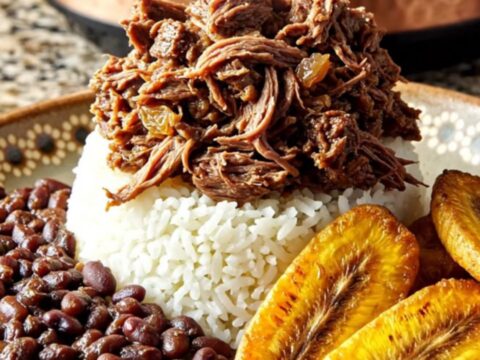 A steaming bowl of Cuban Picadillo with shredded sirloin, golden raisins, and olives served over white rice.