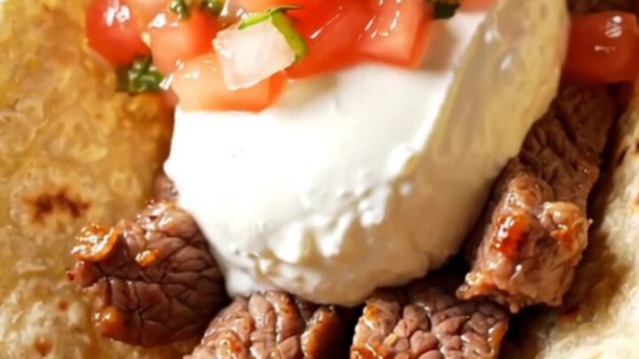 A glossy black Crockpot filled with sizzling tequila lime skirt steak and colorful bell peppers.