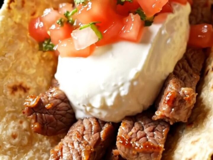 A glossy black Crockpot filled with sizzling tequila lime skirt steak and colorful bell peppers.