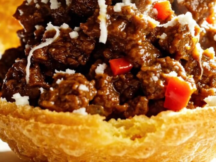 Close-up of shredded beef being pulled with two forks in a white ceramic slow cooker.