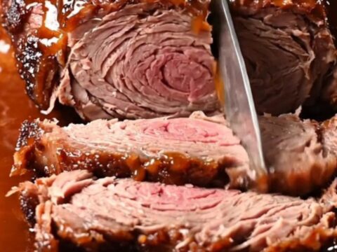 Close-up of a slow-cooked brisket being pulled apart with two forks, showing a dark bark and glossy glaze.