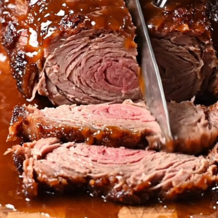 Close-up of a slow-cooked brisket being pulled apart with two forks, showing a dark bark and glossy glaze.