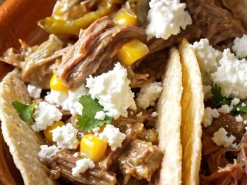 A rustic ceramic slow cooker filled with shredded beef, roasted poblano peppers, and sweet corn in a creamy sauce.