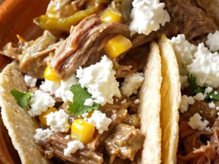 A rustic ceramic slow cooker filled with shredded beef, roasted poblano peppers, and sweet corn in a creamy sauce.