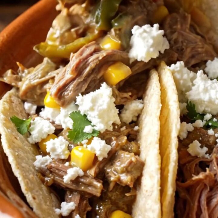 A rustic ceramic slow cooker filled with shredded beef, roasted poblano peppers, and sweet corn in a creamy sauce.