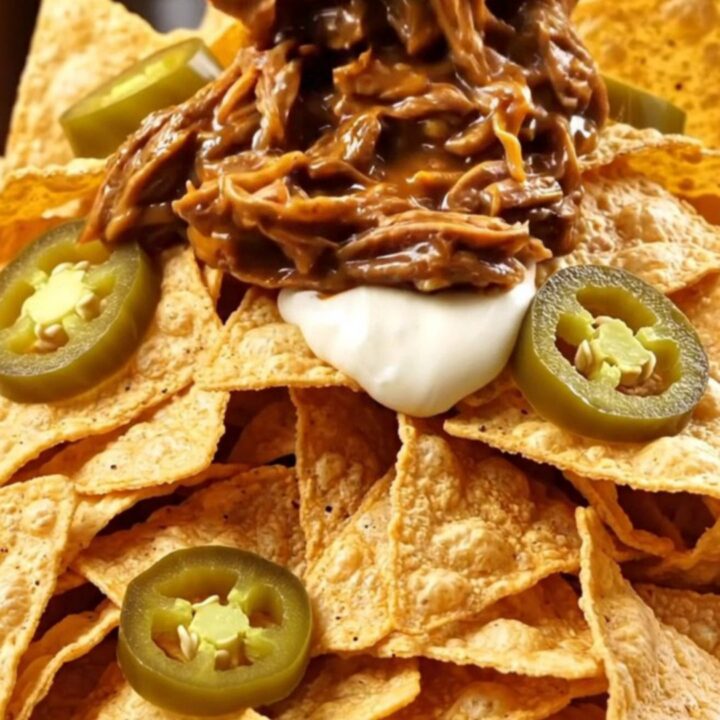 A close-up shot of shredded beef and chorizo in molten queso being lifted with two forks from a black Crockpot.