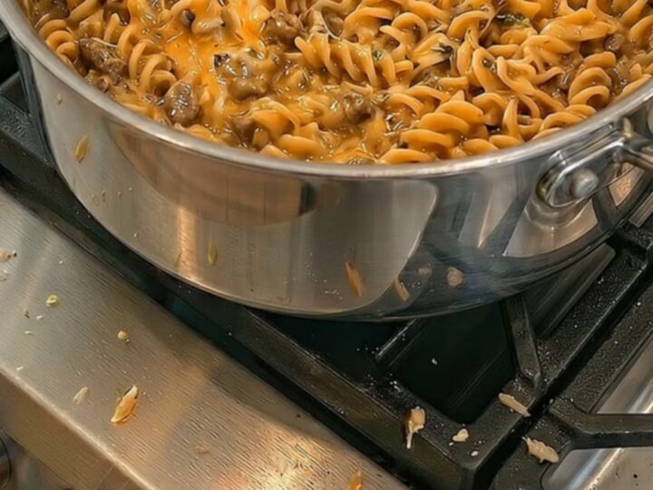 A close-up of a spoon lifting cheesy, creamy rotini pasta from a pot with steam rising and an intense cheese pull.