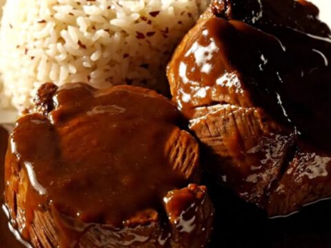 A close-up of a glossy, dark glazed beef roast sliced into medallions in a mahogany ceramic slow cooker.