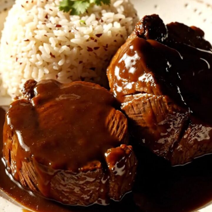 A close-up of a glossy, dark glazed beef roast sliced into medallions in a mahogany ceramic slow cooker.