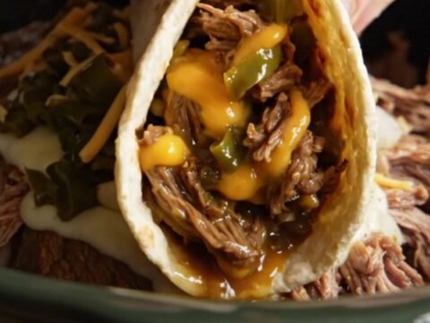A close-up of a slow-cooked shredded beef burrito filled with melted Monterey Jack cheese and Hatch green chiles.