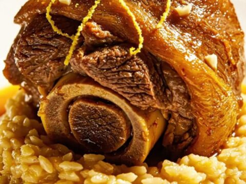 A close-up of a slow-cooked beef shank served on a bed of golden saffron risotto, topped with fresh green gremolata.