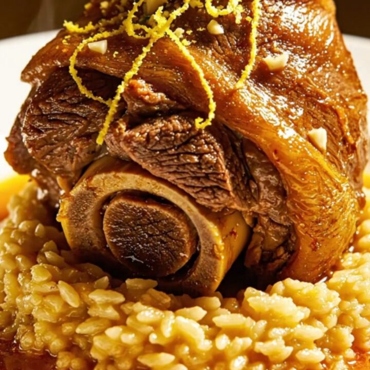 A close-up of a slow-cooked beef shank served on a bed of golden saffron risotto, topped with fresh green gremolata.