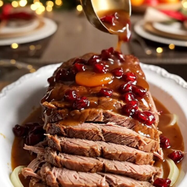 A festive beef brisket fanned out on a white platter, covered in a glossy, mahogany-colored apricot and cranberry gravy.