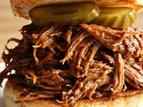 Extreme close-up of root beer braised pulled brisket being lifted with two forks, revealing glossy, sticky barbecue texture.