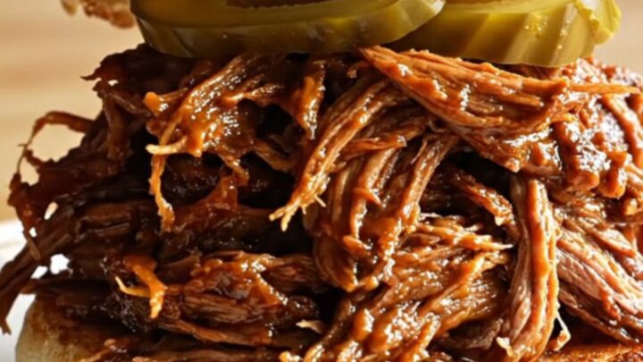 Extreme close-up of root beer braised pulled brisket being lifted with two forks, revealing glossy, sticky barbecue texture.