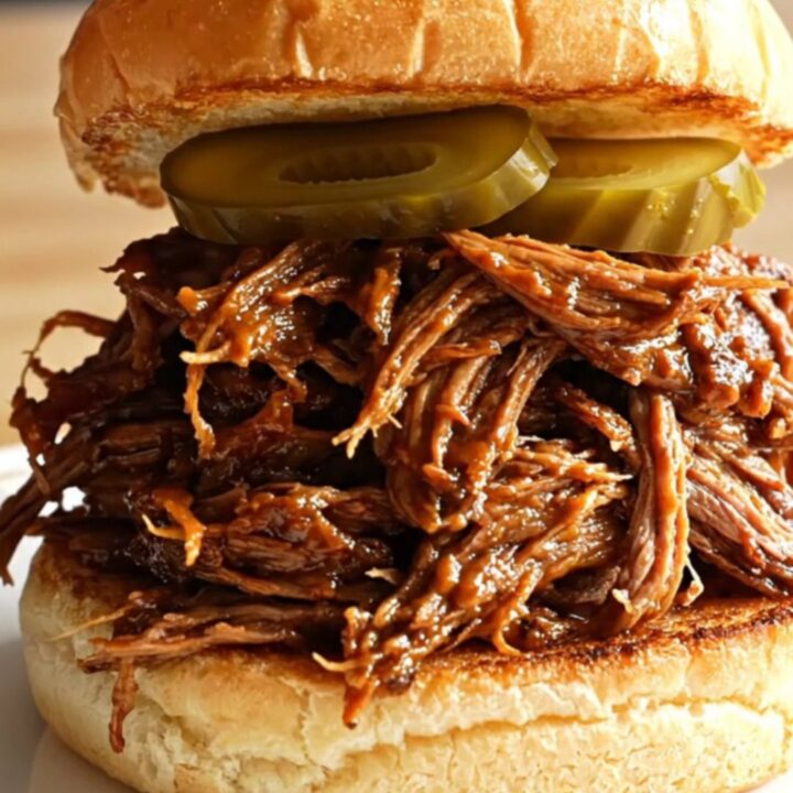Extreme close-up of root beer braised pulled brisket being lifted with two forks, revealing glossy, sticky barbecue texture.