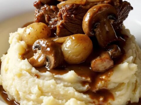A close-up of tender beef short ribs in a rich, mahogany sauce with pearl onions and mushrooms in a Crockpot.