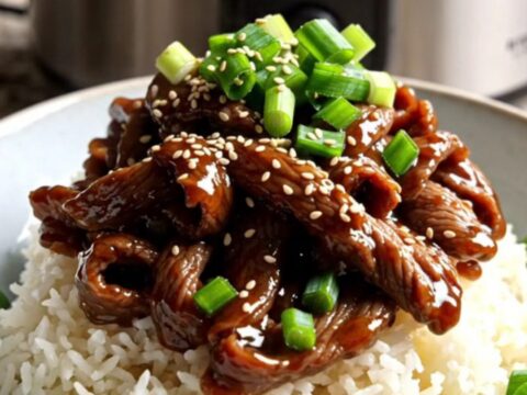 A close-up of tender Mongolian beef ribbons with scallions served over jasmine rice in a modern kitchen.