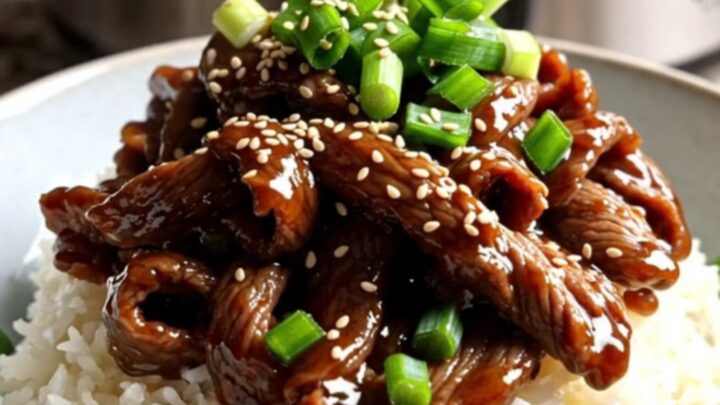 A close-up of tender Mongolian beef ribbons with scallions served over jasmine rice in a modern kitchen.