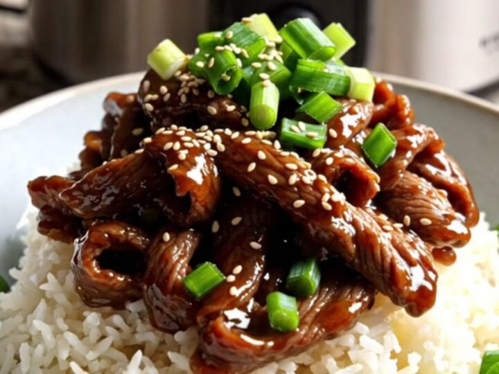 A close-up of tender Mongolian beef ribbons with scallions served over jasmine rice in a modern kitchen.