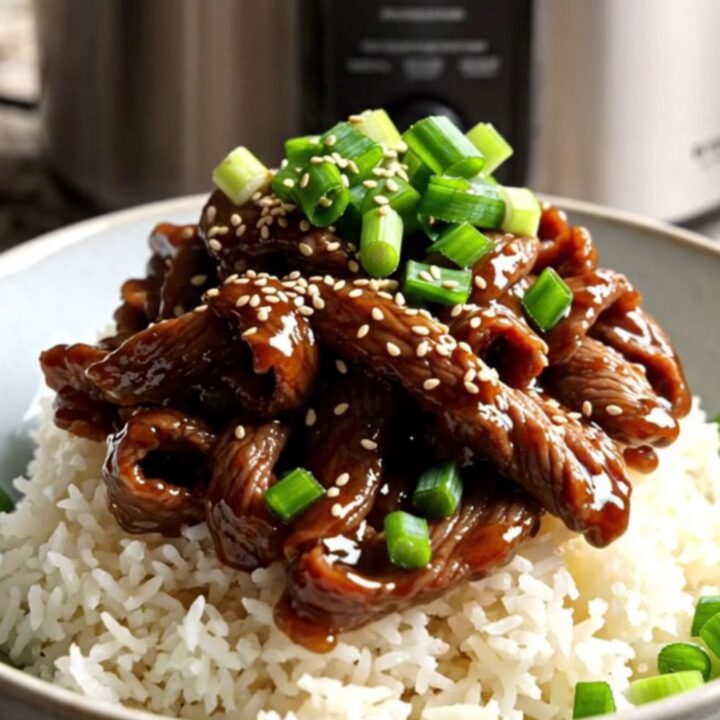 A close-up of tender Mongolian beef ribbons with scallions served over jasmine rice in a modern kitchen.
