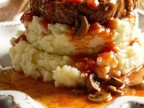 A warm bowl of tender Swiss steak in rich mushroom gravy served over creamy mashed potatoes.
