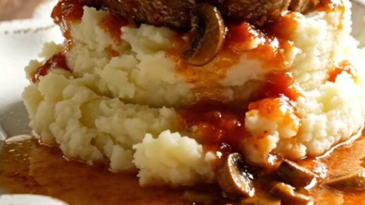 A warm bowl of tender Swiss steak in rich mushroom gravy served over creamy mashed potatoes.