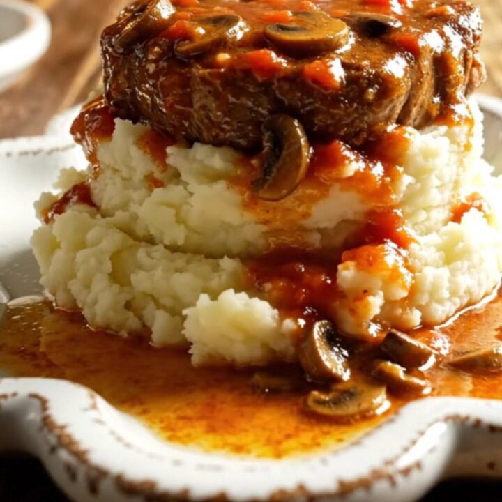 A warm bowl of tender Swiss steak in rich mushroom gravy served over creamy mashed potatoes.