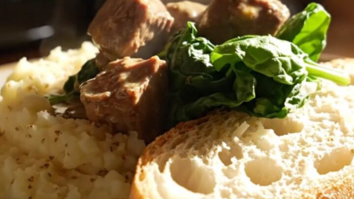 A close-up of creamy Tuscan steak bites in a ceramic slow cooker with visible spinach and sun-dried tomatoes.