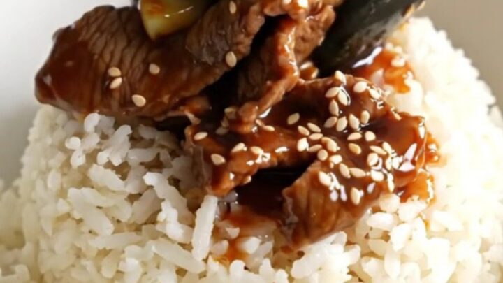 A close-up of glossy beef and broccoli in a dark ceramic slow cooker.