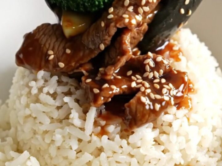 A close-up of glossy beef and broccoli in a dark ceramic slow cooker.