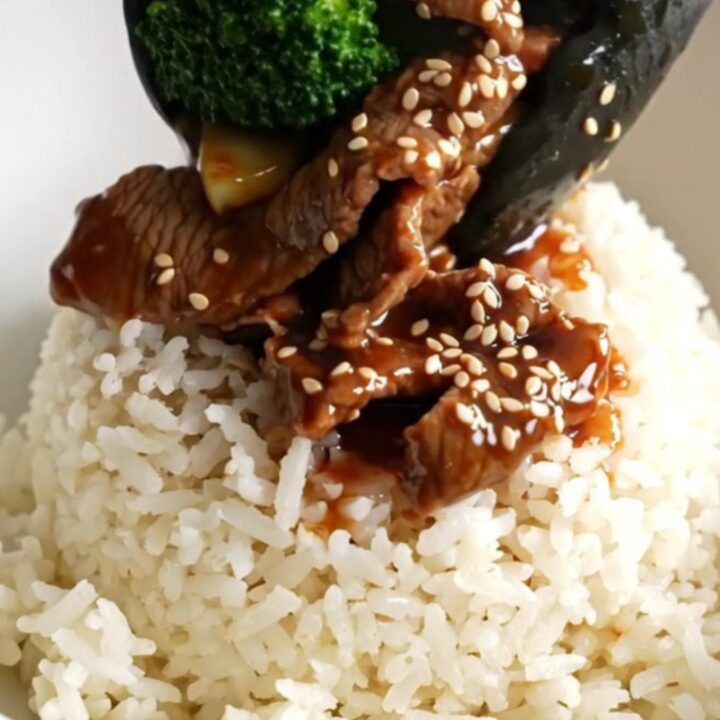 A close-up of glossy beef and broccoli in a dark ceramic slow cooker.