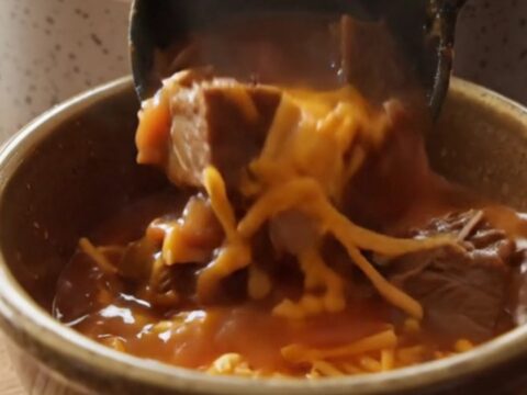 A warm stoneware bowl filled with hearty Shipwreck beef stew, topped with melted sharp cheddar cheese.