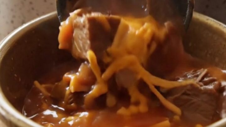 A warm stoneware bowl filled with hearty Shipwreck beef stew, topped with melted sharp cheddar cheese.