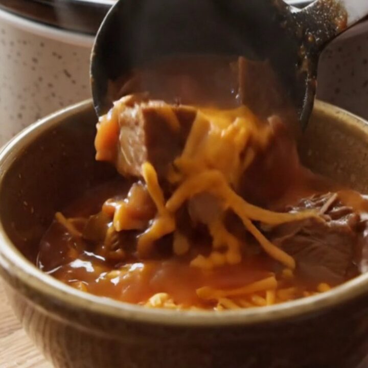 A warm stoneware bowl filled with hearty Shipwreck beef stew, topped with melted sharp cheddar cheese.