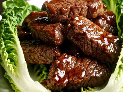 Close-up of caramelized Bulgogi steak tips being lifted from a black ceramic slow cooker with chopsticks.